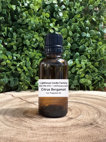 1 oz. Citrus Bergamot fragrance oil by The Lighthouse Candle Factory in an amber glass bottle with a black, tamper-evident dropper cap, set against a greenery background.