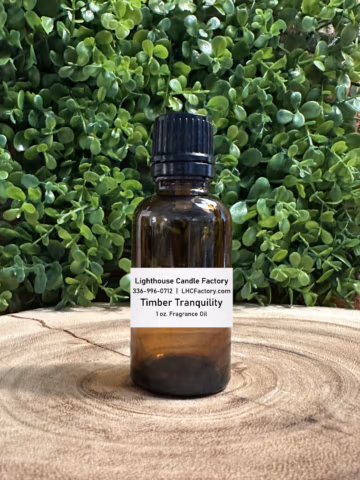 1 oz. Timber Tranquility fragrance oil by The Lighthouse Candle Factory in an amber glass bottle with a black, tamper-evident dropper cap, set against a greenery background.
