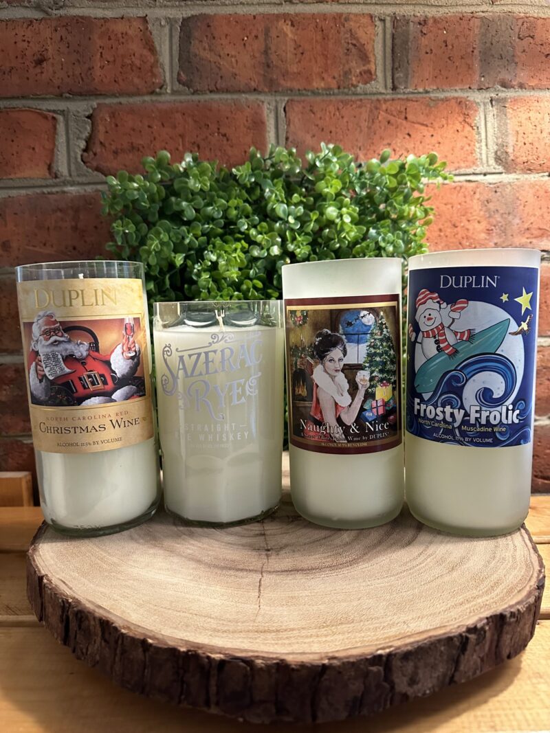 Custom bottle candles featuring upcycled holiday bottles like Duplin Christmas Wine, Sazerac Rye, Naughty and Nice, and Frosty Frolic, showcasing seasonal wine bottle candle cutting. A perfect exanple of our custom candles.