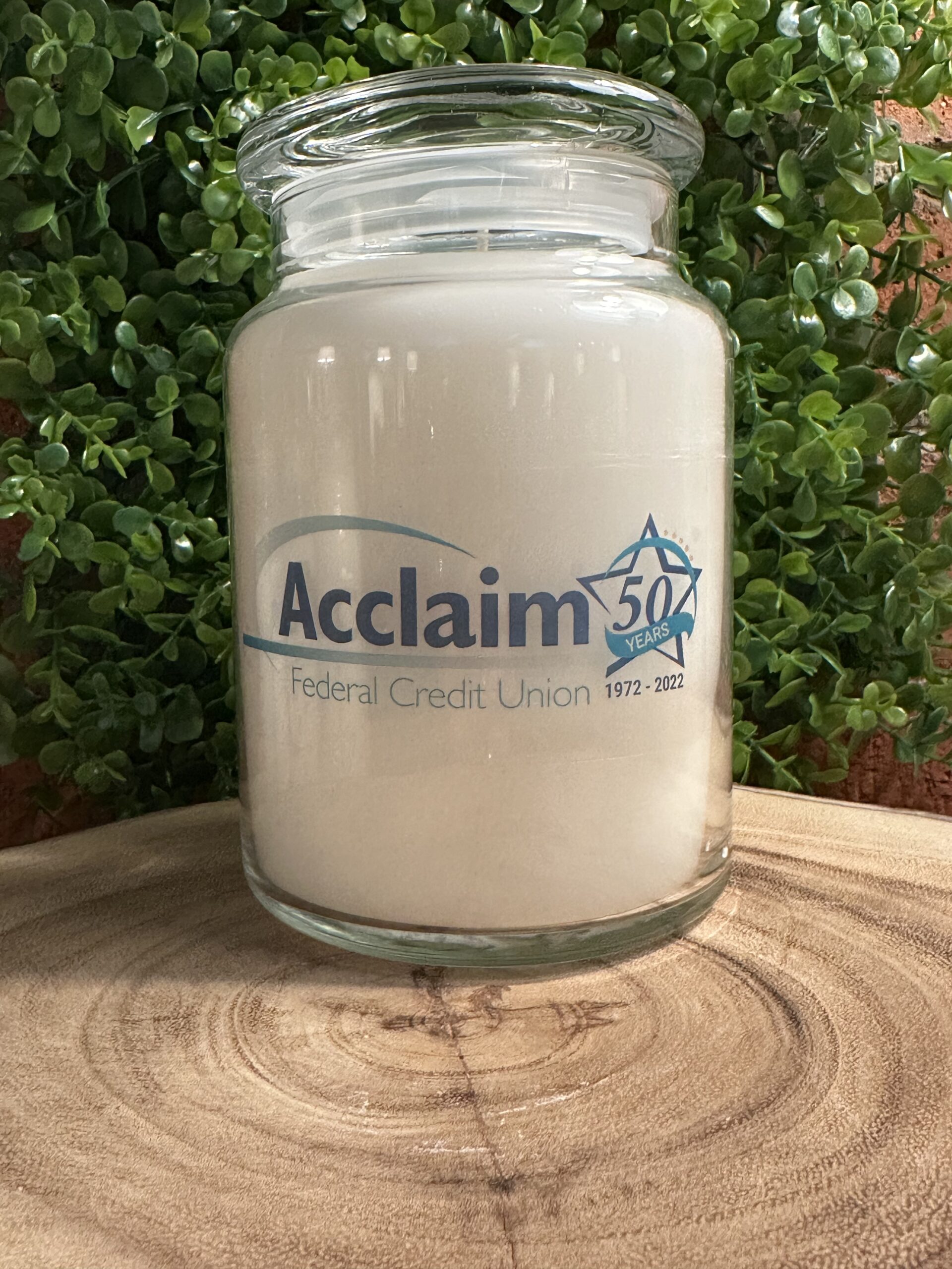 One of The Lighthouse Candle Factory's Custom Corporate Candle Gifts inside a clear glass jar with white wax featuring the Acclaim Federal Credit Union 50th Anniversary logo.