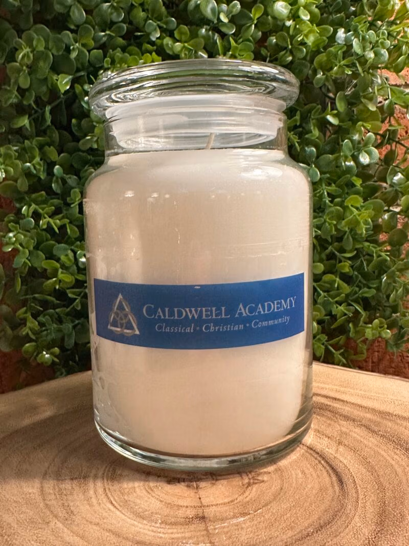 One of The Lighthouse Candle Factory's Custom Corporate Candle Gifts inside a clear glass jar with white wax featuring the Caldwell Academy logo.