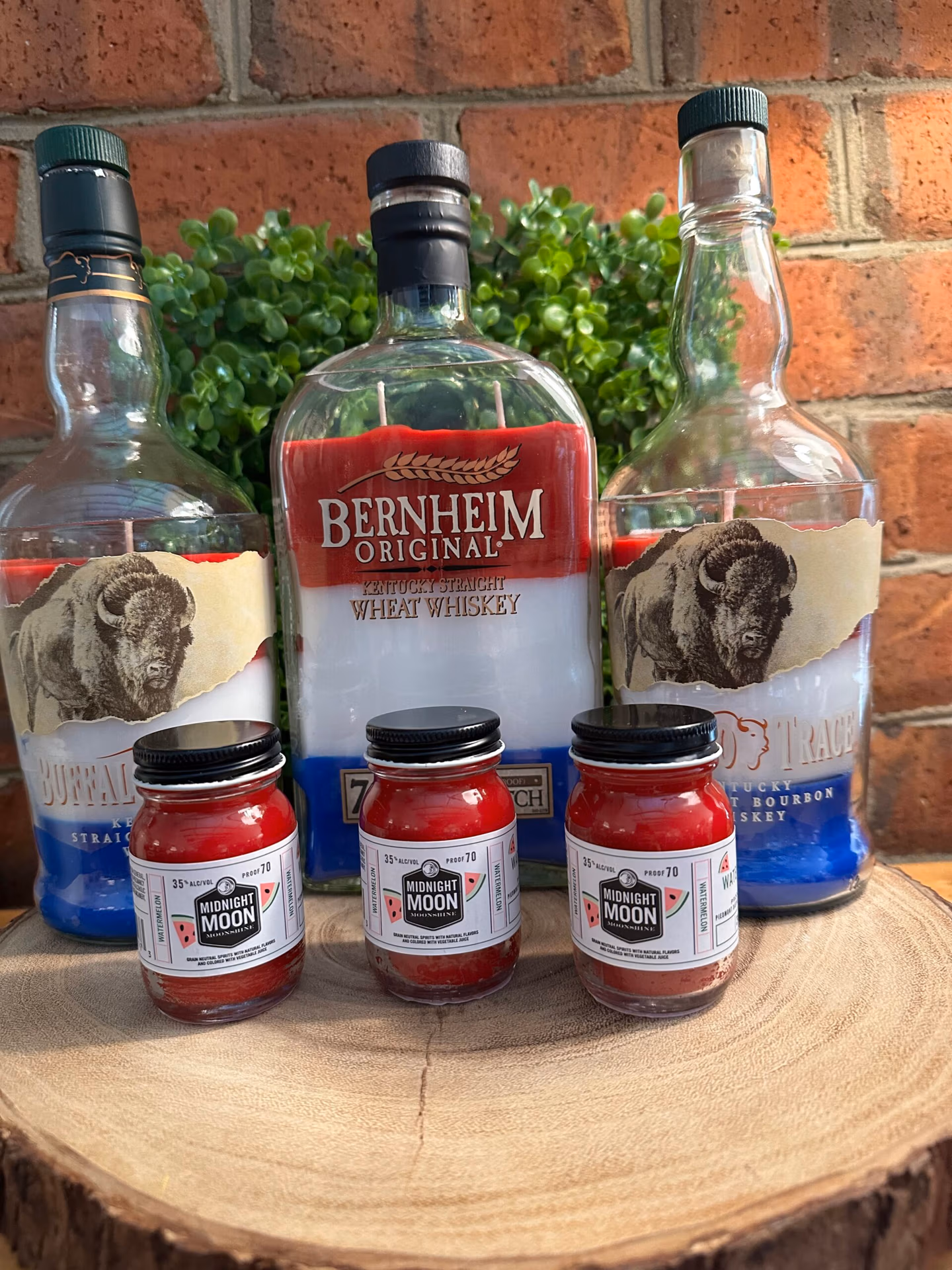 Custom bottle candles made from upcycled Buffalo Trace, Bernheim Original, and Midnight Moon moonshine bottles featuring red, white, and blue layered wax, demonstrating The Lighthouse Candle Factory's custom bottle cutting program.