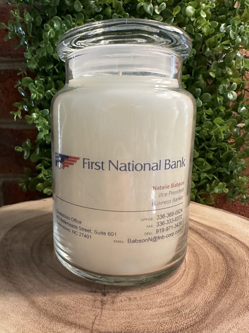 One of The Lighthouse Candle Factory's Custom Corporate Candle Gifts inside a clear glass jar with white wax featuring the First National Bank logo.