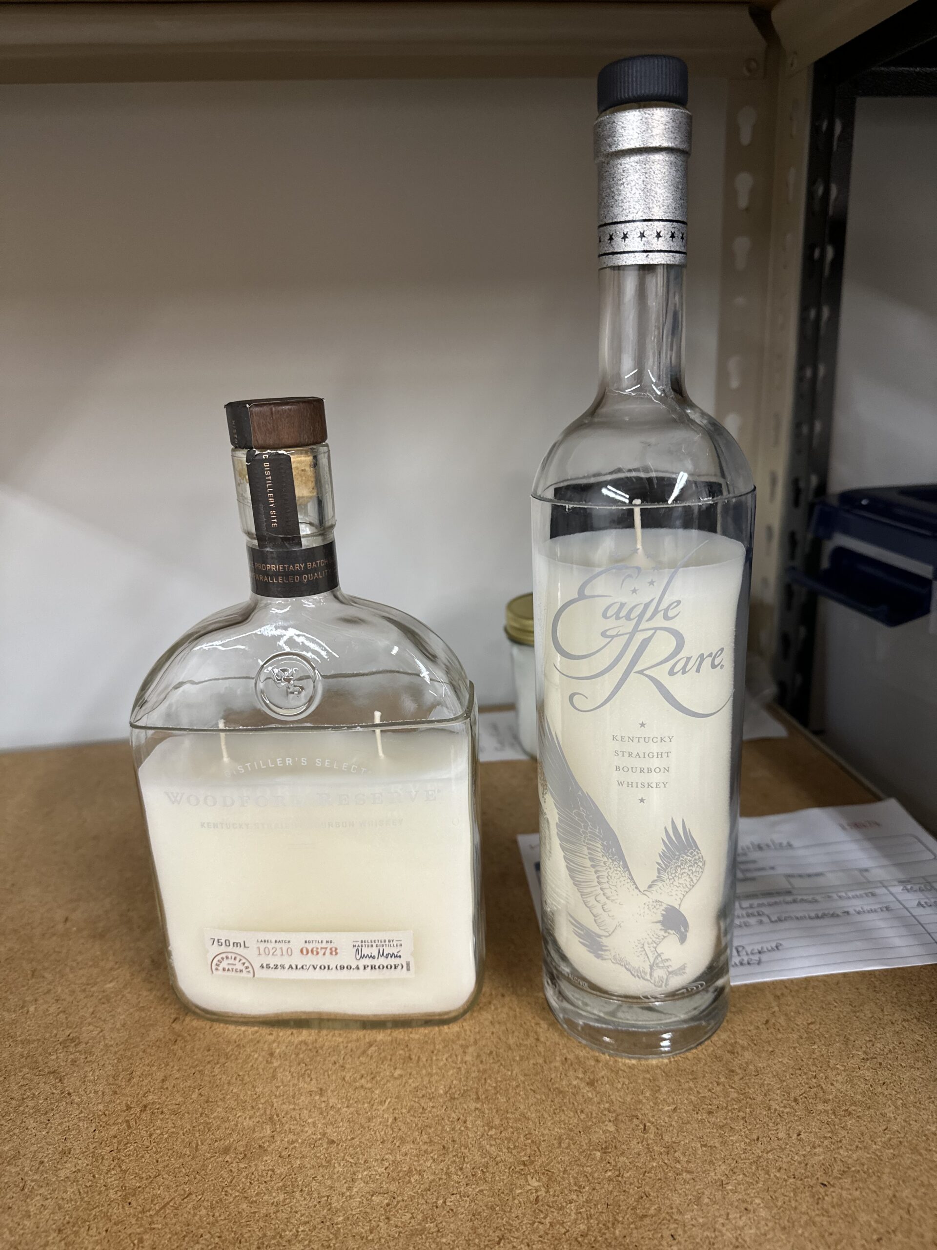 Custom bottle candles crafted from upcycled Woodford Reserve bourbon and Eagle Rare whiskey bottles with elegant white wax, showcases premium liquor bottle upcycling.