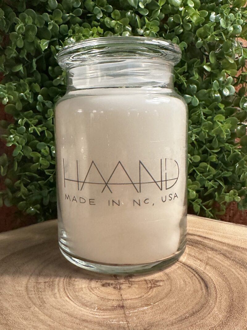 One of The Lighthouse Candle Factory's Custom Corporate Candle Gifts inside a clear glass jar with white wax featuring the HAAND logo.