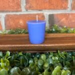 A purple votive from The Lighthouse Candle Factory on a beautiful wooden display with greenery.