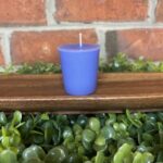 A purple votive from The Lighthouse Candle Factory on a beautiful wooden display with greenery.