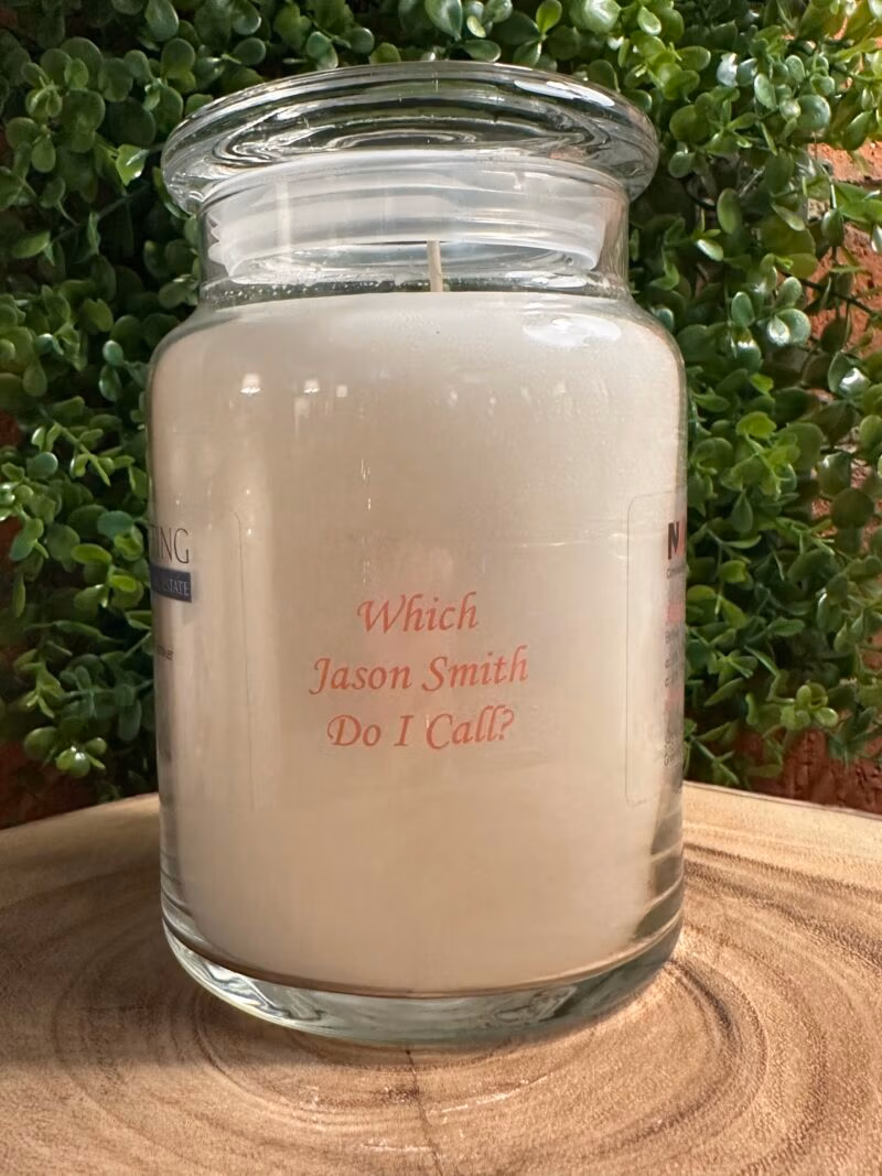 One of The Lighthouse Candle Factory's Custom Corporate Candle Gifts inside a clear glass jar with white wax featuring the Jason Smith logo.