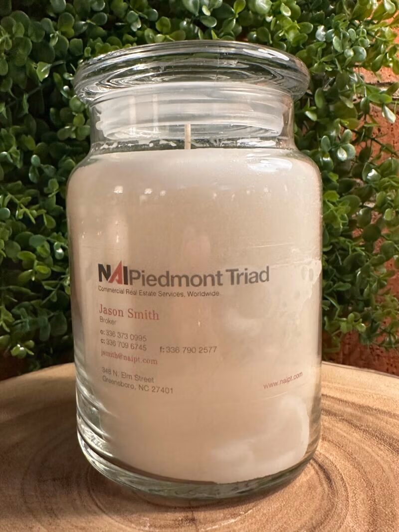 One of The Lighthouse Candle Factory's Custom Corporate Candle Gifts inside a clear glass jar with white wax featuring the Jason Smith logo.