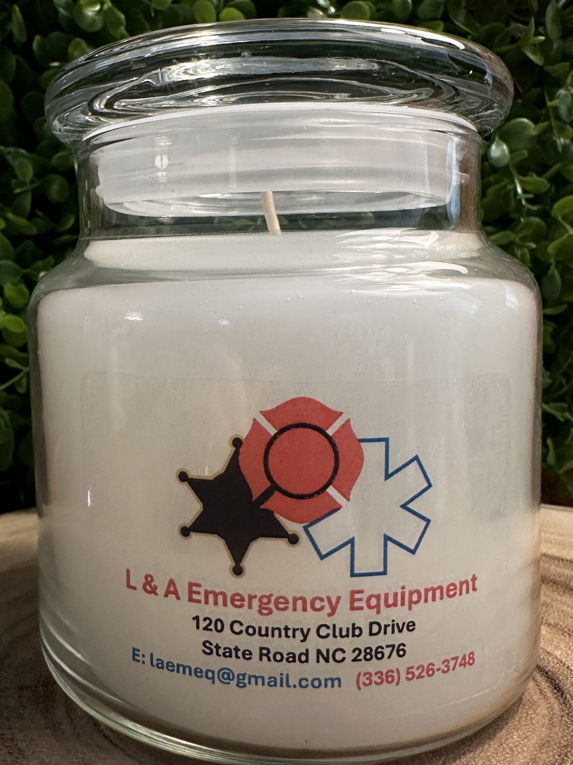 One of The Lighthouse Candle Factory's Custom Corporate Candle Gifts inside a clear glass jar with white wax featuring the L&A Emergency Equipment logo.