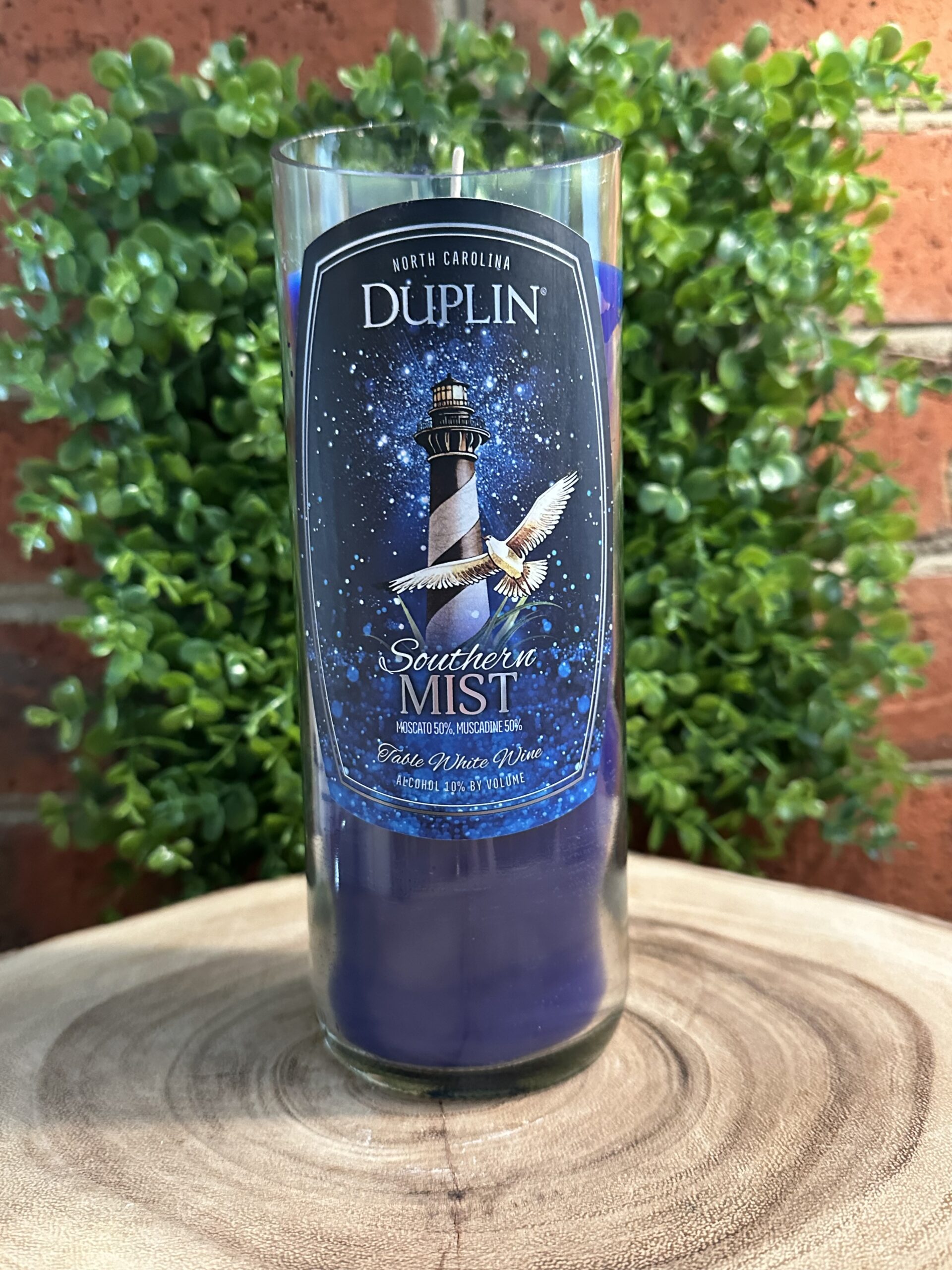 Custom bottle candles created from an upcycled Duplin Winery Southern Mist wine bottle filled with dark blue wax, highlighting premium glass bottle cutting service results.