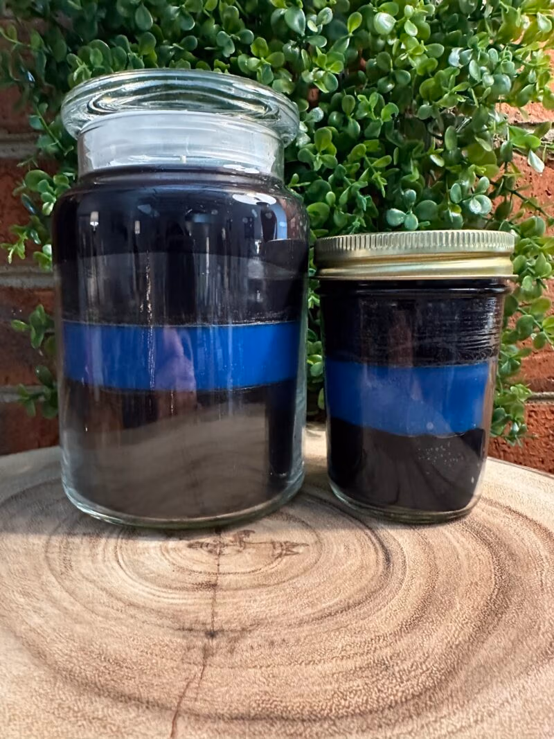 The Thin Blue Line custom candles in a glass apothecary jar and a mason jar, showcasing hand-poured custom candles from The Thin Line Collection for first responders and charity programs.