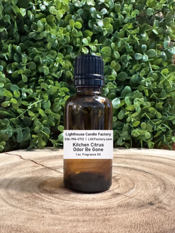 1 oz. Kitchen Citrus Odor Be Gone (OBG) fragrance oil by The Lighthouse Candle Factory in an amber glass bottle with a black, tamper-evident dropper cap, set against a greenery background.