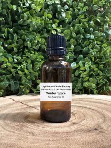 1 oz. Winter Spice fragrance oil by The Lighthouse Candle Factory in an amber glass bottle with a black, tamper-evident dropper cap, set against a greenery background.
