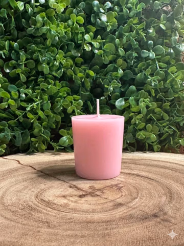Almond vanilla votive candle with pink wax and a single wick on a wood surface