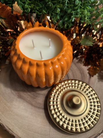 Pumpkin Pie Scented Candle with three unlit wicks and pale cream-colored wax in a glossy orange pumpkin-shaped vessel beside a gold lid
