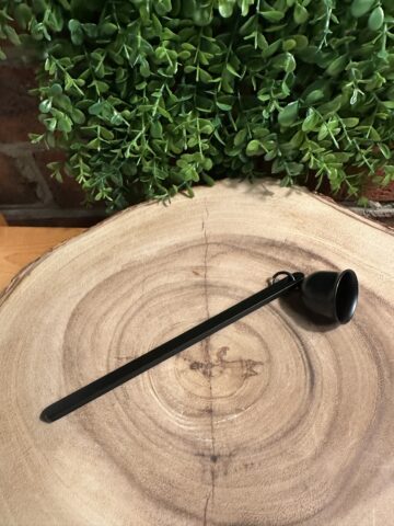 Matte black candle snuffer with a bell-shaped head resting on a cross-section wood slice background.