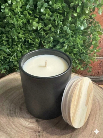 Amazing Grace floral musk candle, unlit in a black ceramic vessel with its lid leaning beside it on a wood slice.