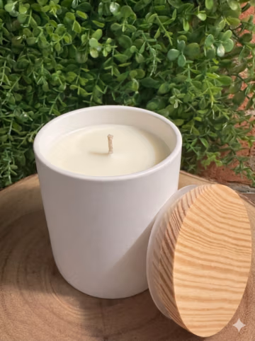 Amazing Grace floral musk candle, unlit in a white ceramic vessel with a wood-grain lid leaning beside it.