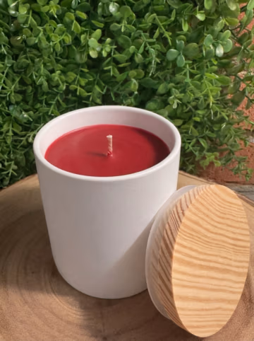 Apple Cinnamon Candle, unlit in a white ceramic vessel with Crimson Red wax and a wood-grain lid leaning beside it.