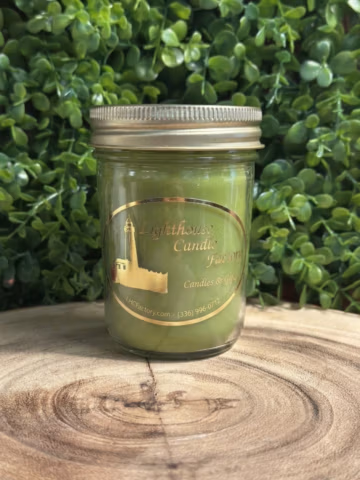 Bayberry scented candle in a clear jelly jar with a gold-tone lid, on a wood slice against green foliage