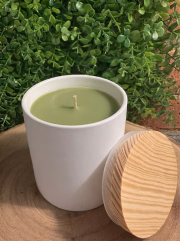 Bayberry scented candle in a white ceramic vessel, unlit with green wax and a wood-grain lid leaning beside it.
