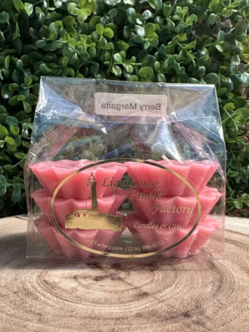 Berry Margarita wax tarts in a clear bag with a gold lighthouse logo, on a wood slice against green foliage