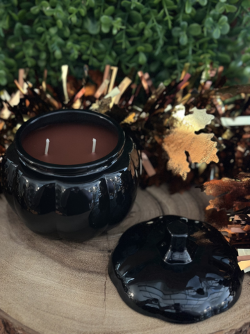 Grandpa's Apple Cider Scented Candle in an open black pumpkin jar with two unlit wicks and its stemmed lid beside it.