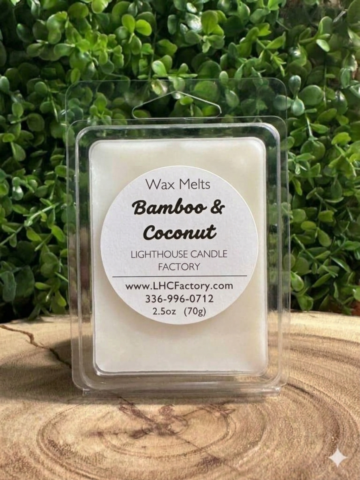 Bamboo and Coconut Wax Melts in a closed clear clamshell on a wood slice against green foliage.