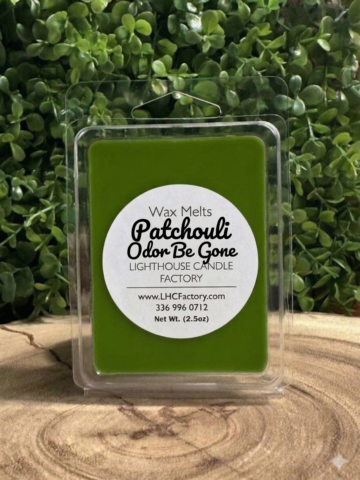 Patchouli wax melts in a closed clear clamshell with a white round label, standing on a wood slice against green foliage.