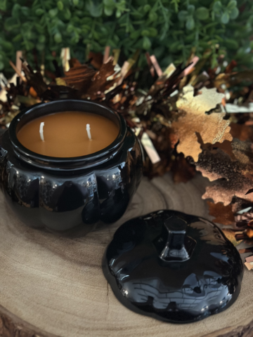Pumpkin Chai Candle in an open black pumpkin jar with two unlit wicks and a matching lid resting beside it.