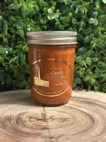 Pumpkin Chai Candle in a jelly jar with a gold lid, shown front-on on a wood slice against green foliage.
